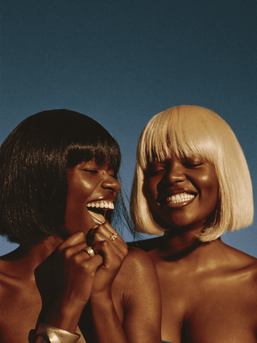 Two Black women laughing together wearing Mane Logiq wigs